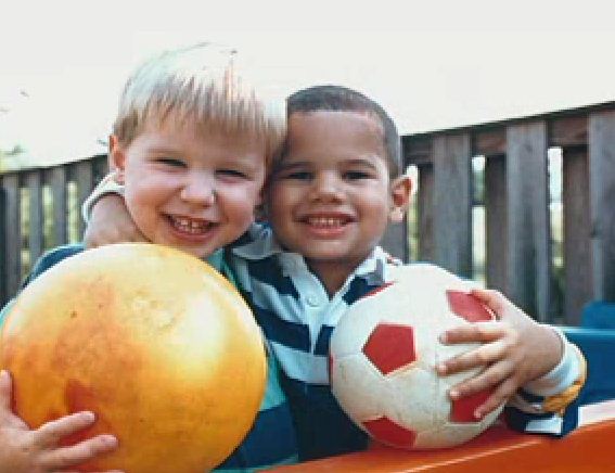  One boy embraces another. Both are smiling each holds a ball.